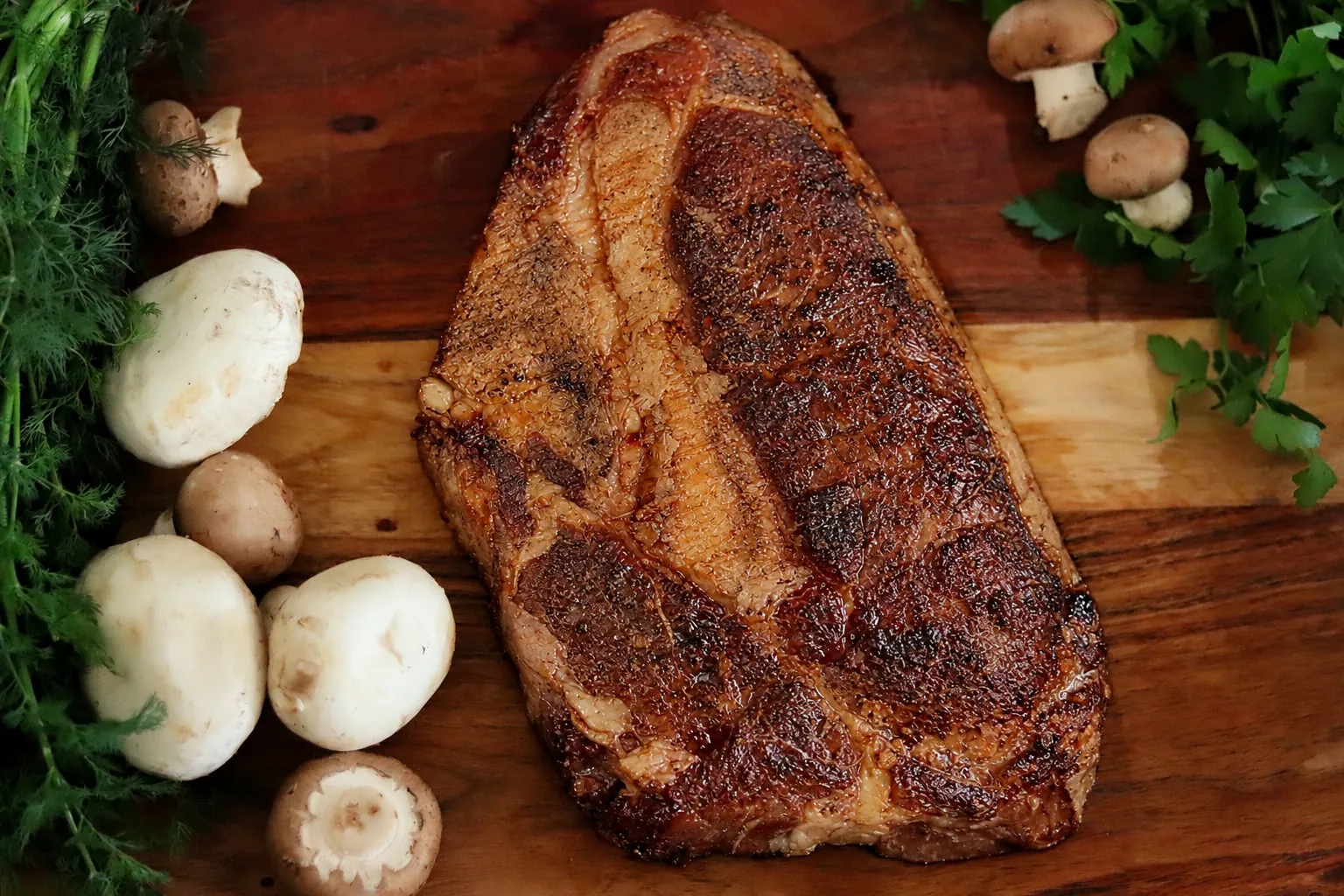 A seared Barton Beef steak on a cutting board with mushrooms and fresh herbs