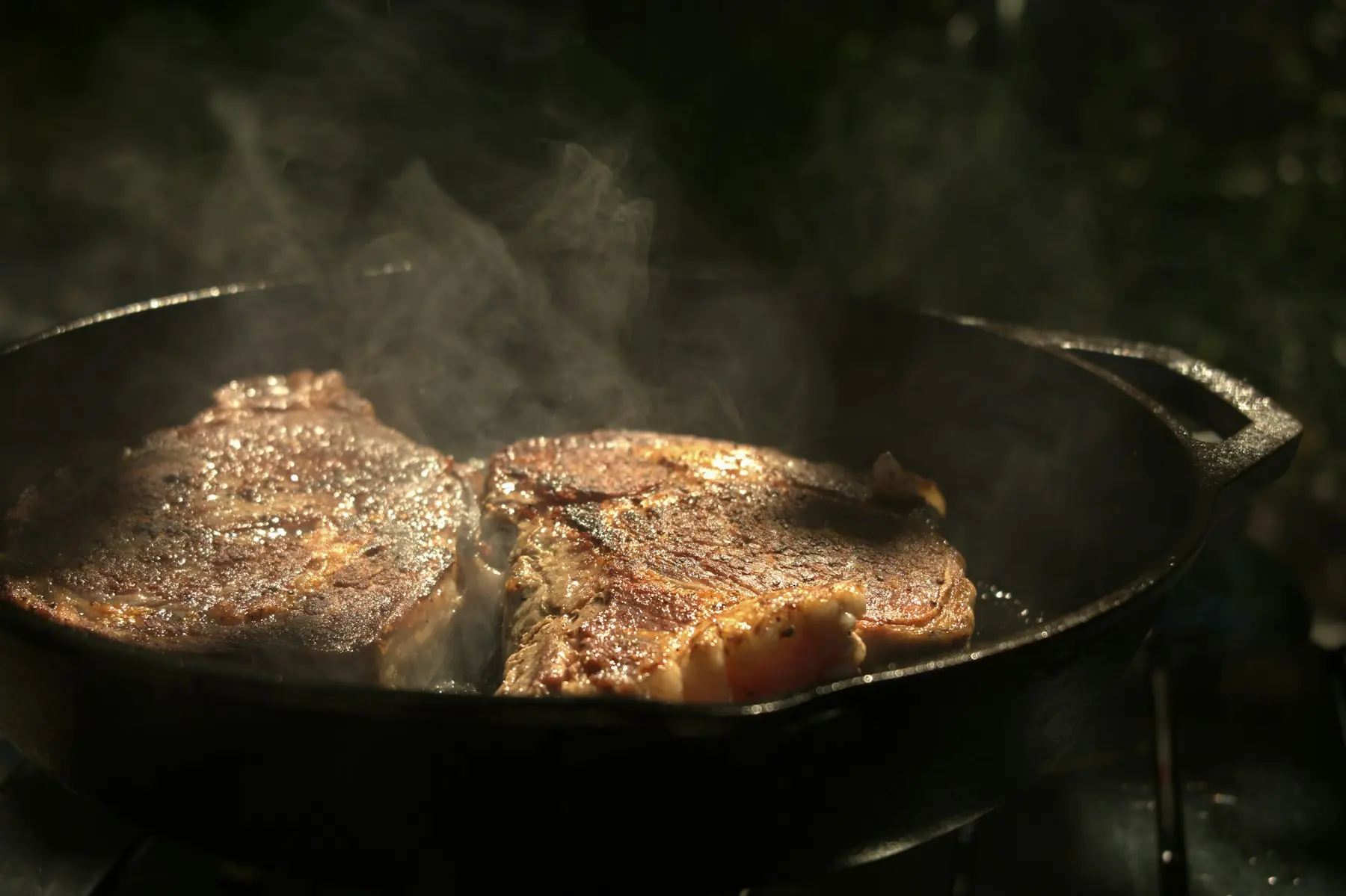 Two steaks searing in a cast iron skillet